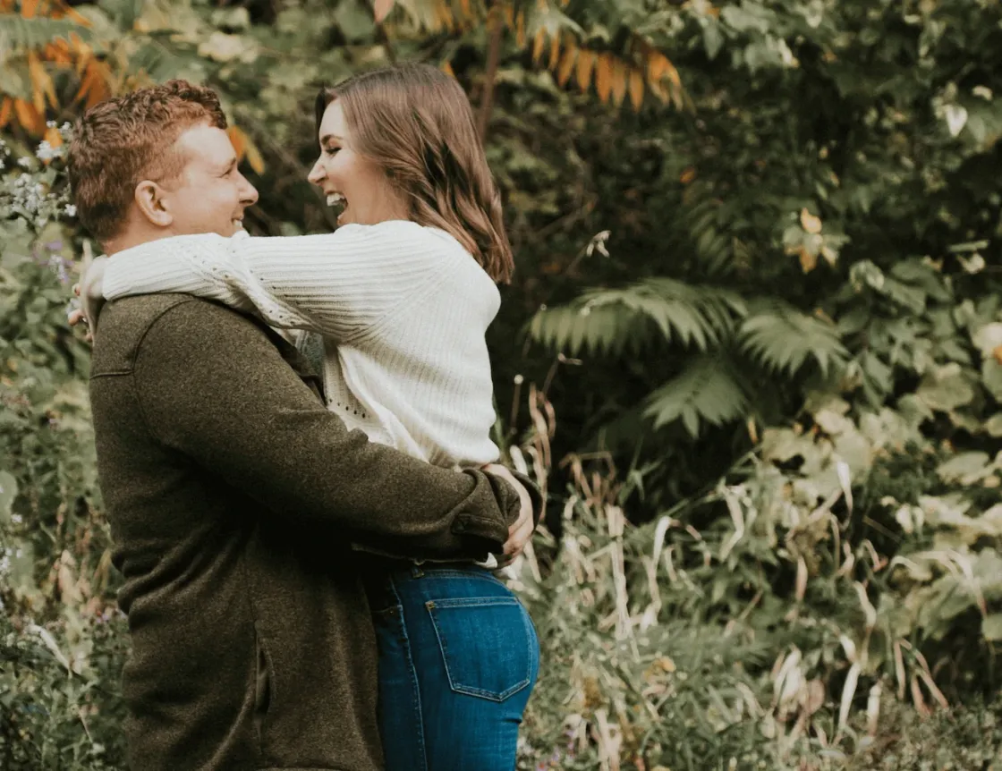 An engaged couple holding hands among trees