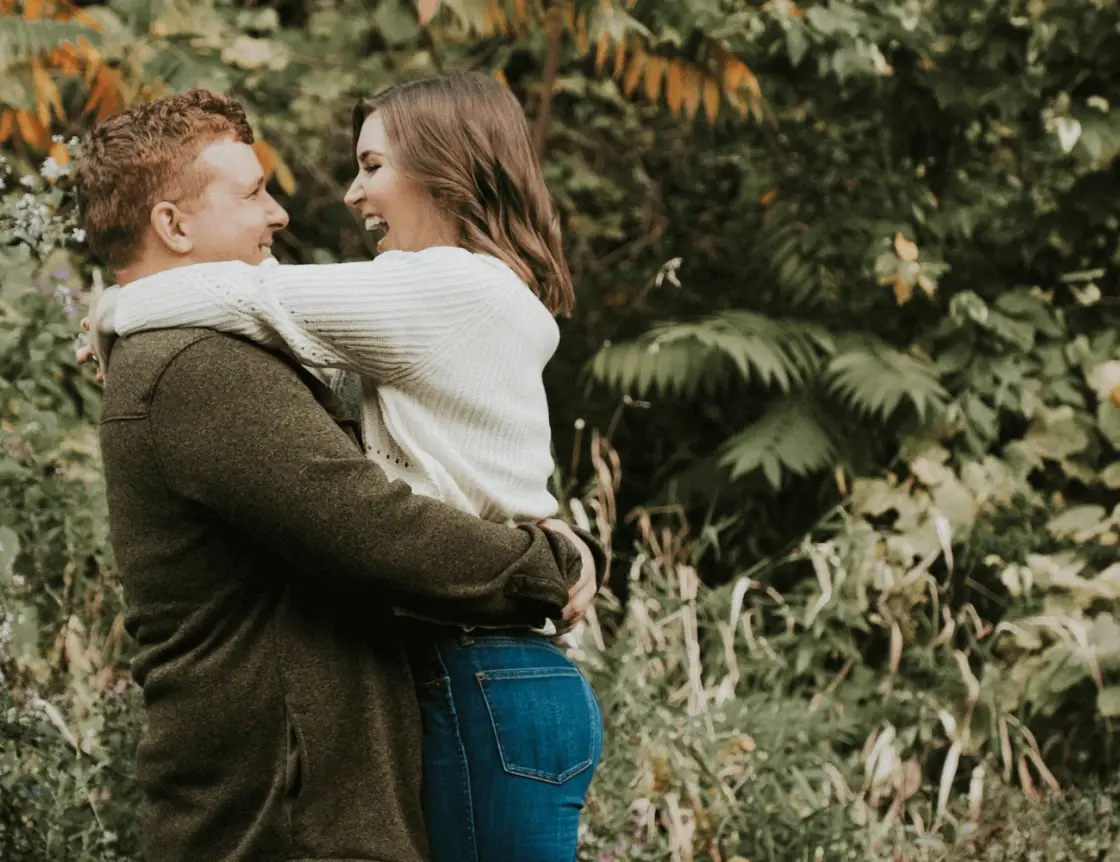 An engaged couple holding hands among trees