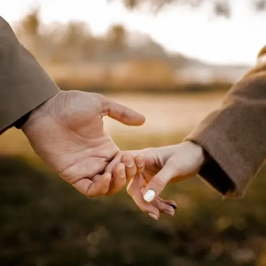 Two hands linked by a little finger, outdoors in warm autumn light