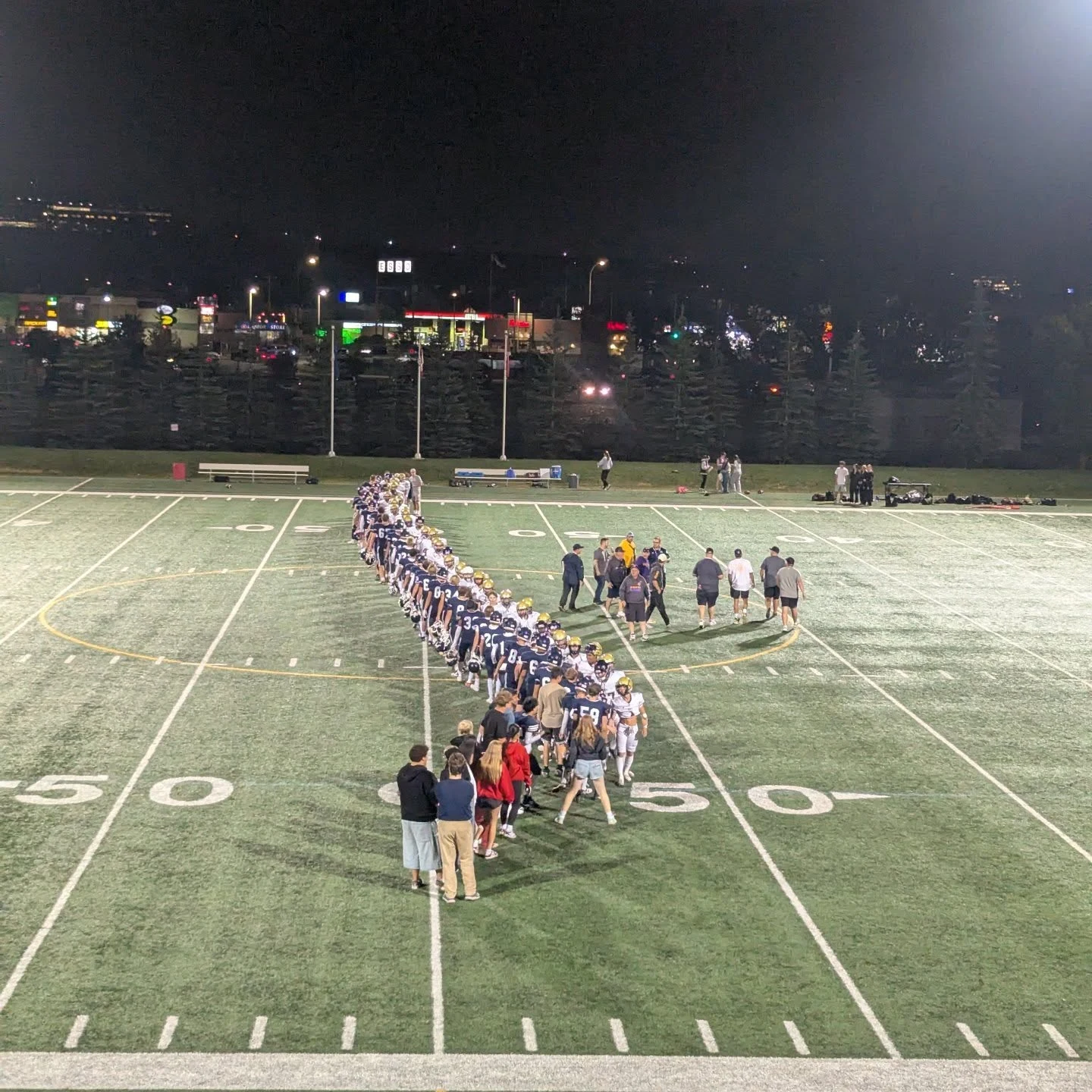 Football players and coaches lined up on a floodlit field at night