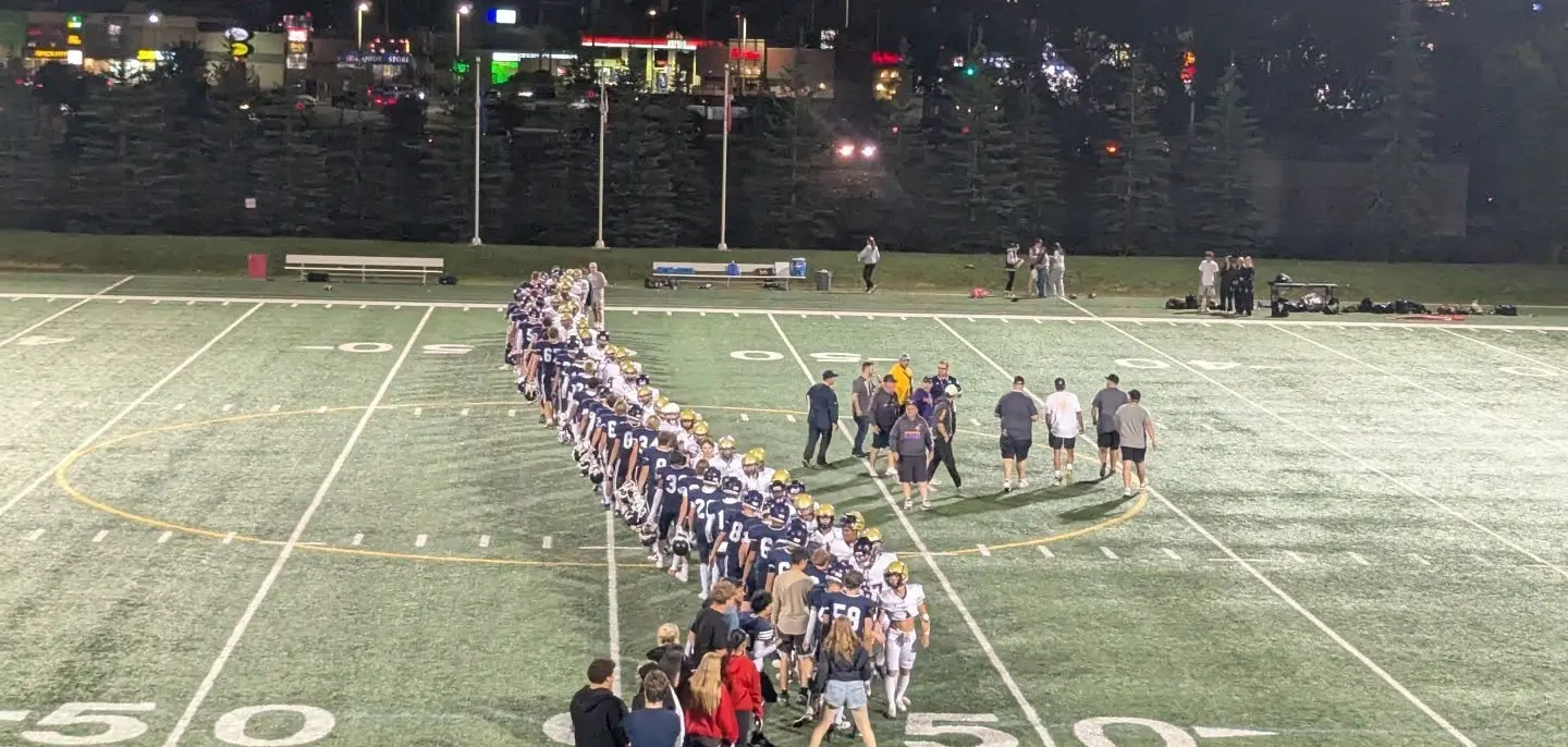 Football players and coaches lined up on a floodlit field at night