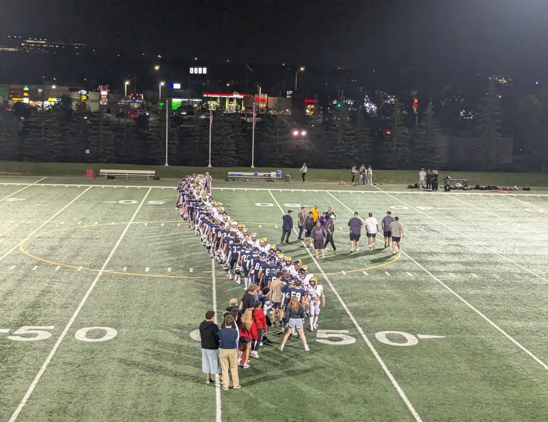 Football players and coaches lined up on a floodlit field at night