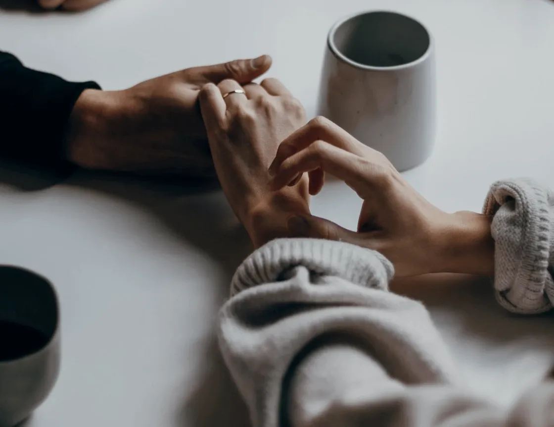 Two people holding hands across a table set with coffee cups
