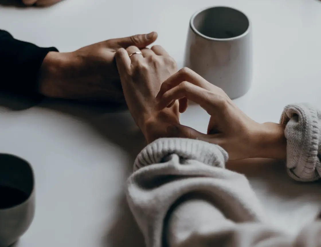 Two people holding hands across a table set with coffee cups