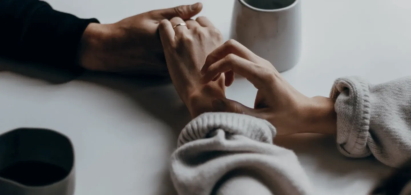 Two people holding hands across a table set with coffee cups