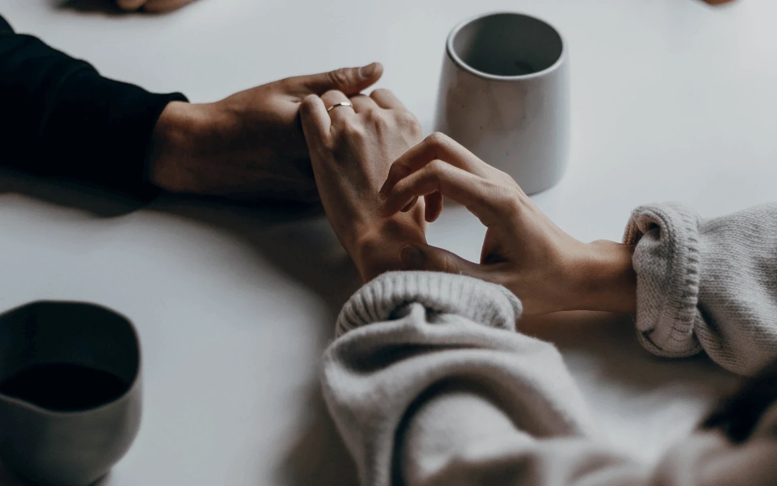 Two people holding hands across a table set with coffee cups